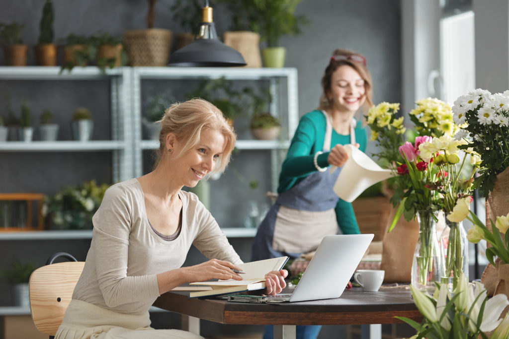 Florist leading small business, sitting beside desk, using laptop