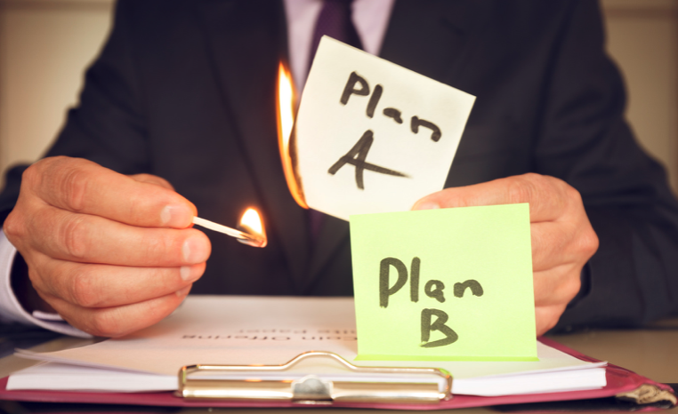 Small business owner in a suit lighting a sticky note with 'Plan A' written on it on fire with a match